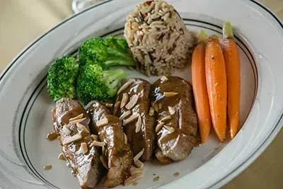 Well-plated entree with sliced meat, carrots, wild rice, and broccoli.