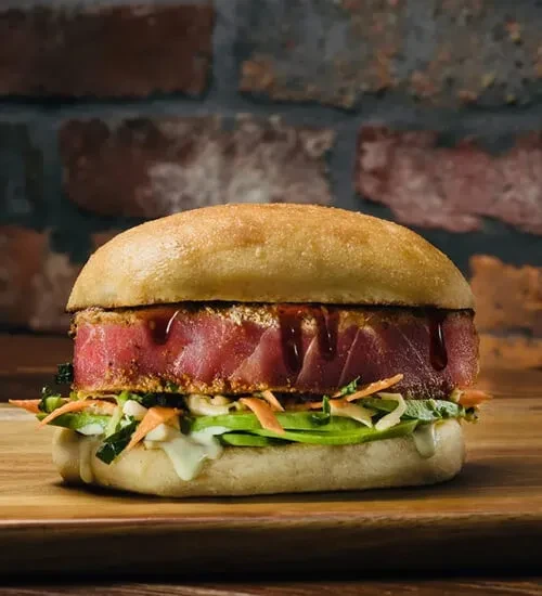 Burger with seared tuna or salmon patty, avocado, carrots, greens.