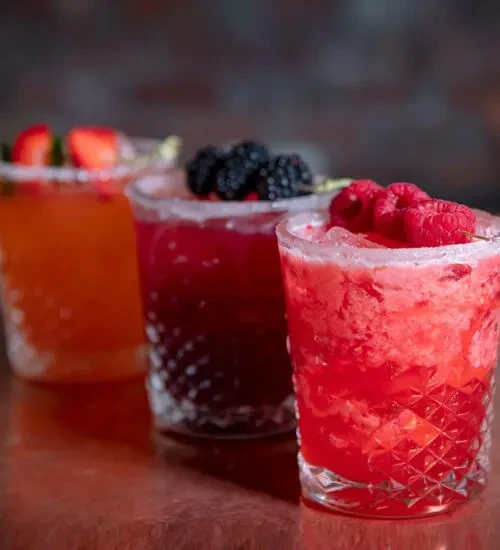 Red, purple, and orange cocktails with berries and sugar rims.