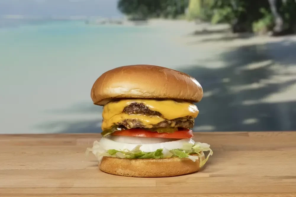 Double cheeseburger with melted cheese and fresh toppings, ocean background.