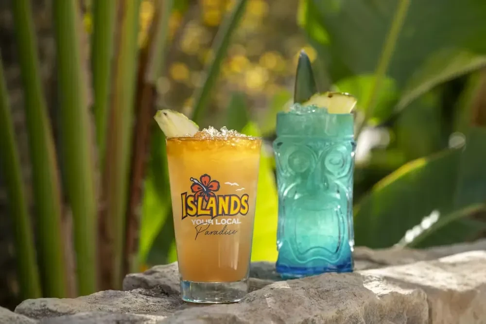 Orange and blue tropical drinks with pineapple, outdoors.