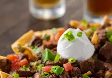 Close-up of loaded nachos with beef, tomatoes, scallions, and sour cream.