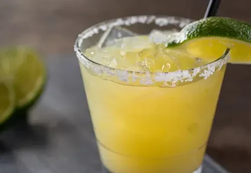 Salt-rimmed yellow-orange cocktail with crushed ice, lime, and straw.