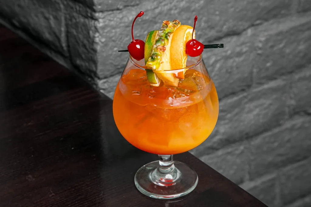 Vibrant orange cocktail in goblet, garnished with fruit on a skewer.