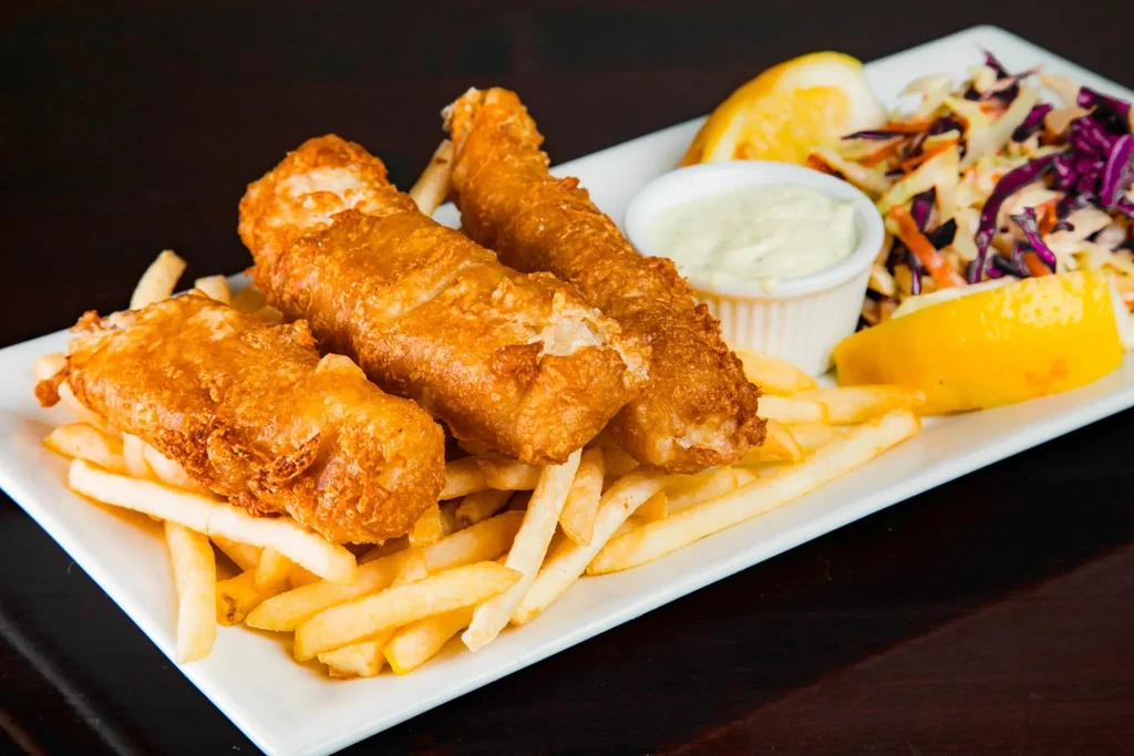 Close-up of fish and chips with tartar sauce, coleslaw, and lemon.