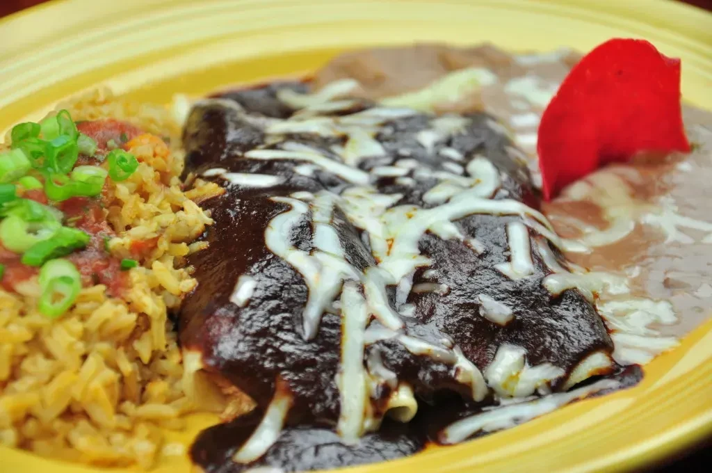 Close-up of mole enchiladas, rice, and refried beans on yellow plate.