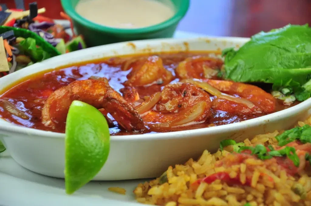 Shrimp in reddish sauce, yellow rice, lime, and blurred Mexican dishes.