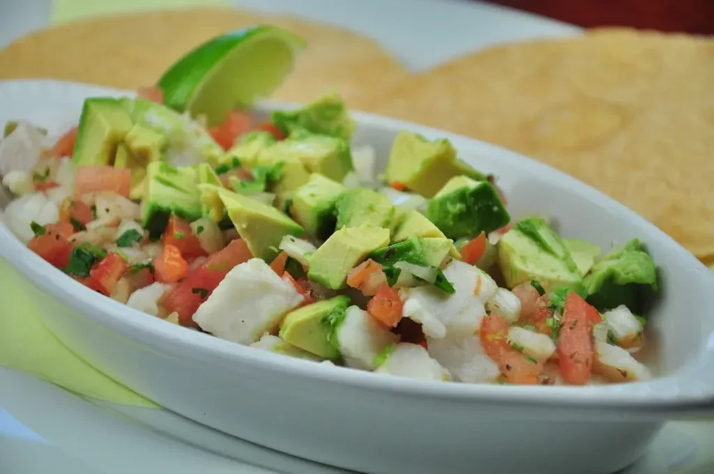 Ceviche with fish, avocado, tomato, onion, cilantro, and a lime wedge.