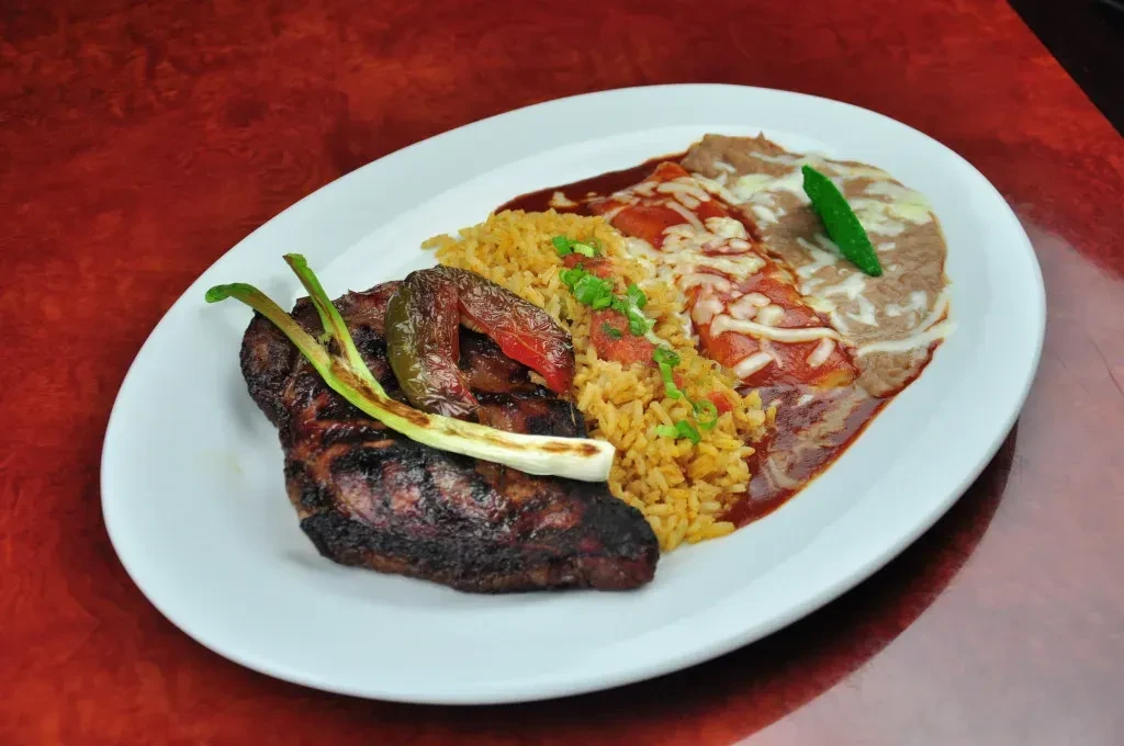 Mexican combo plate: grilled meat, enchiladas, rice, and refried beans.
