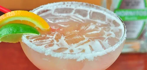 Pale pink cocktail with salted rim, orange slice, and lime wedge.