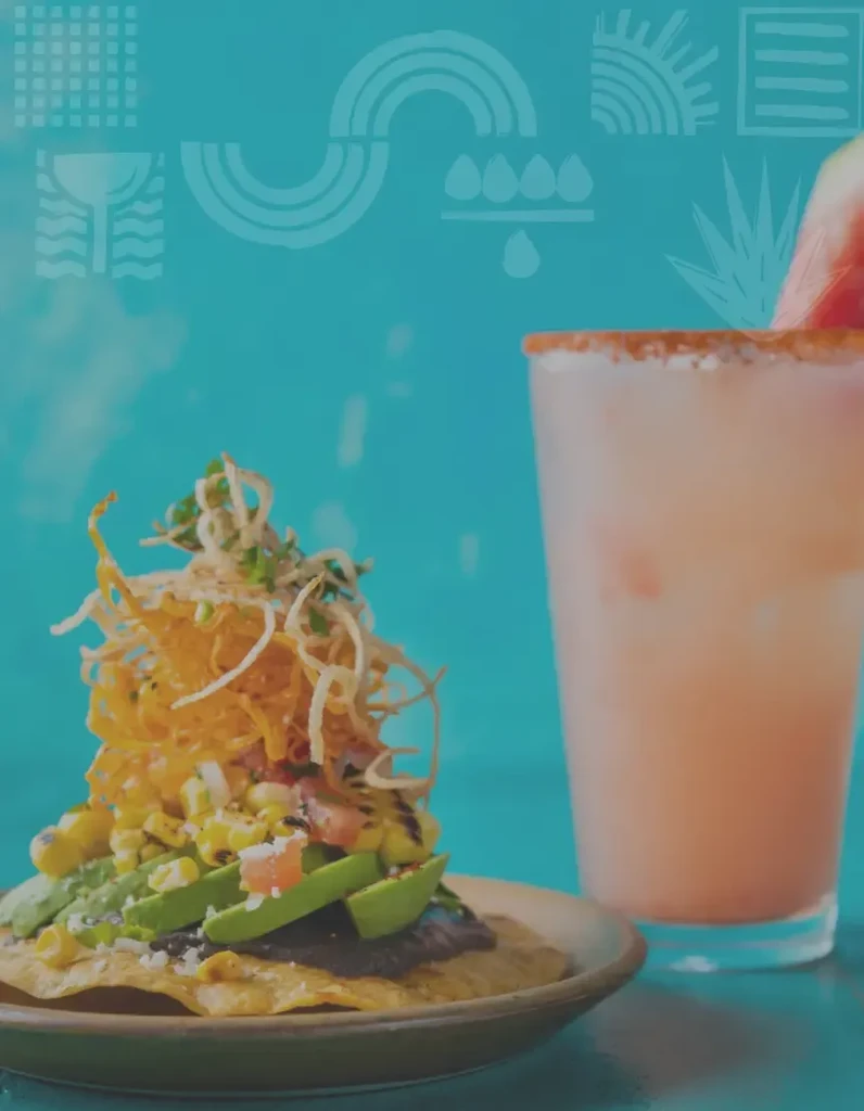 Colorful tostada and pink drink with fruit on a teal background.