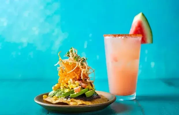 Colorful stacked tostada, pink drink with chili-salt rim on turquoise.