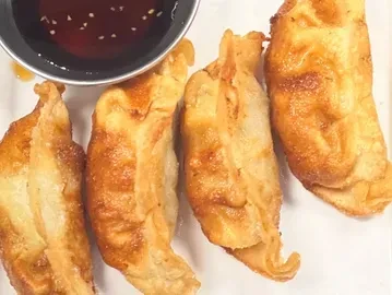 Four golden-brown fried dumplings with dark dipping sauce and sesame seeds.