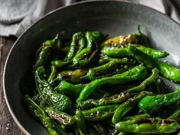 Close-up: dark ceramic bowl of charred green peppers with sea salt.
