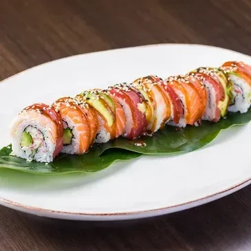 Plated sushi pieces with salmon, tuna, avocado, sesame, dark sauce.