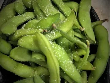 Close-up of a pile of vibrant green edamame pods with coarse salt.