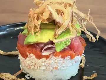 Layered poke tower with rice, crab, tuna, avocado, and crispy onions.