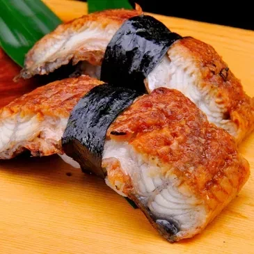 Three glazed unagi nigiri with nori on a wooden surface.