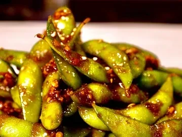 Green edamame pods glazed in reddish-brown sauce, sprinkled with sesame seeds.