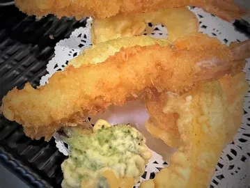 Crispy shrimp and vegetable tempura with doilies on a black serving tray.