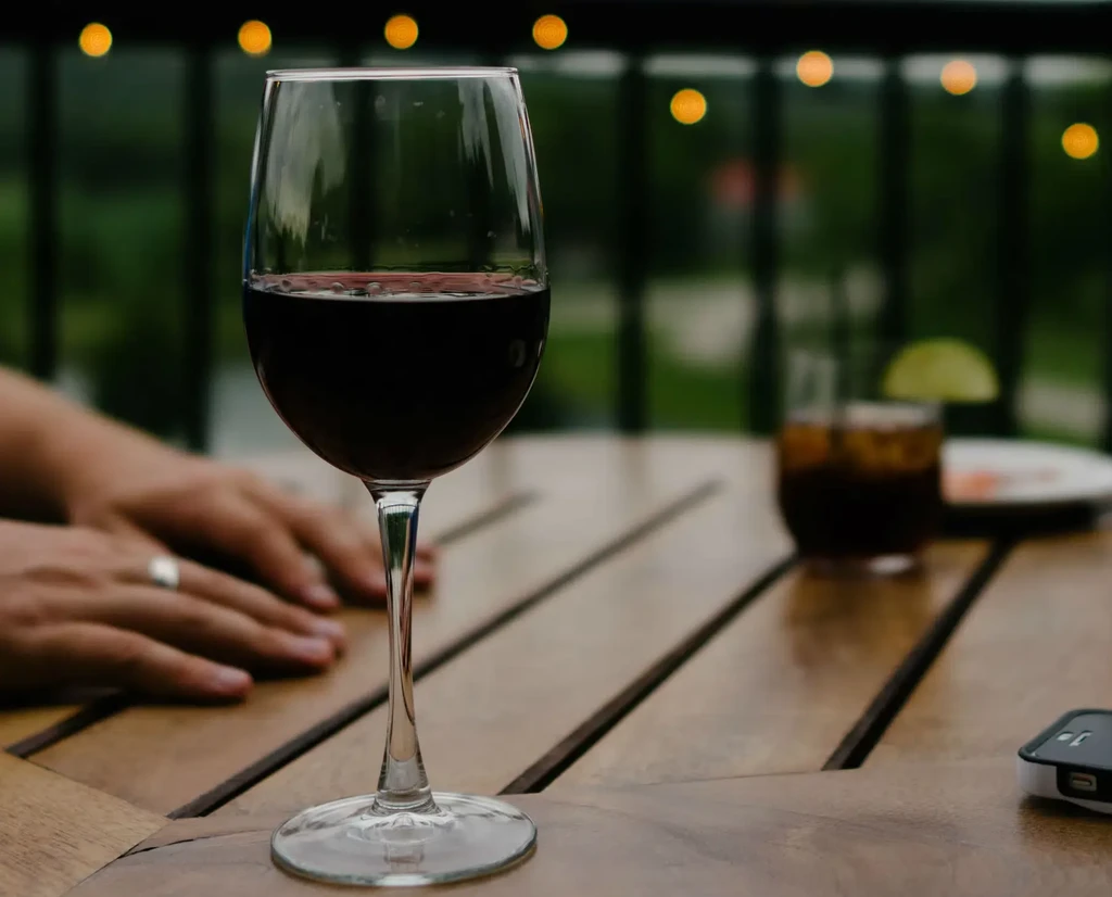 Half-full glass of red wine on table with blurred evening bokeh background.
