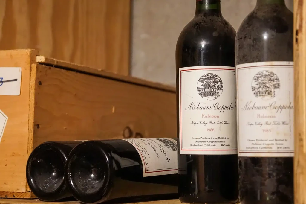 Four dusty Niebaum-Coppola 'Rubicon' 1985 and 1986 wine bottles in a cellar.