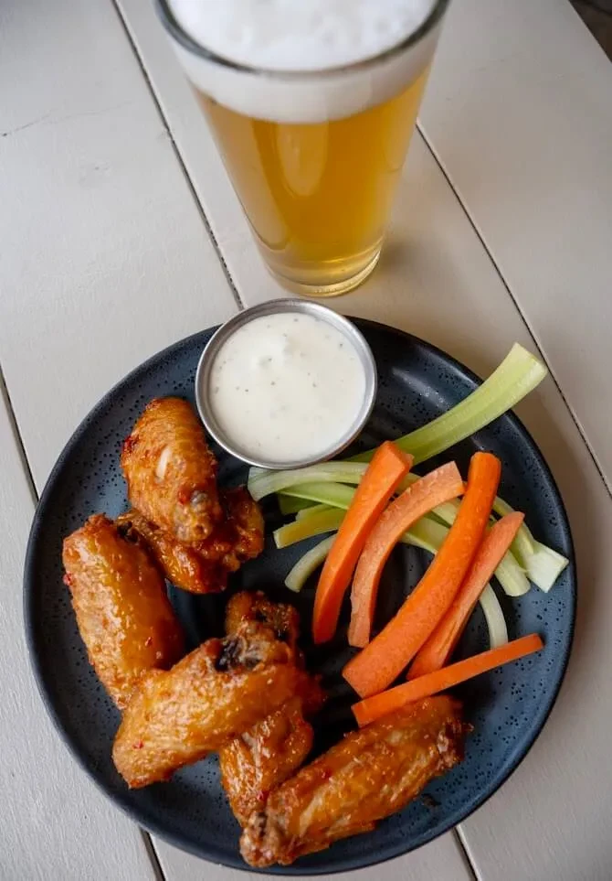 Overhead view: Sauced chicken wings, raw vegetables, white dip, foamy beer.