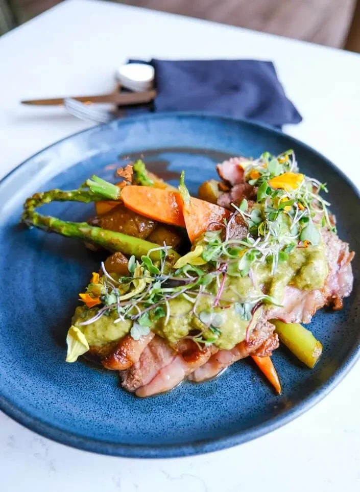 Artfully plated gourmet meal: sliced meat, green sauce, roasted vegetables.