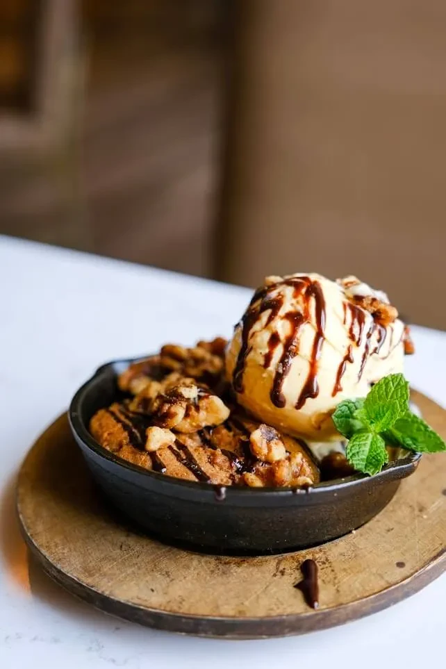 Warm baked dessert in a skillet with ice cream, chocolate, nuts, and mint.