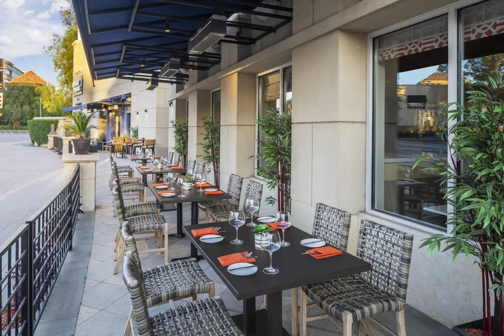 Set outdoor dining patio with orange napkins, woven chairs, and blue awning.