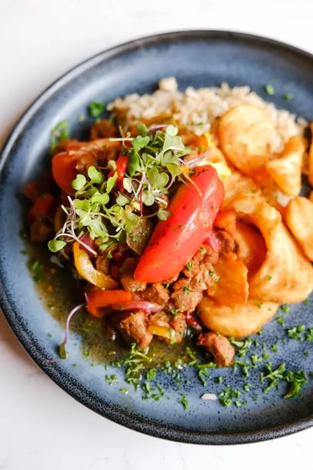 Close-up of stewed beef, peppers, microgreens, fried bread, and grain.