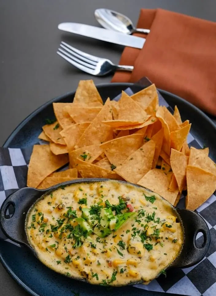 Elote corn dip with avocado and herbs, surrounded by tortilla chips.