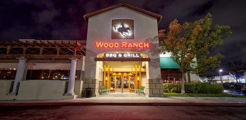 Wood Ranch BBQ & Grill exterior at night, with neon sign and logo.