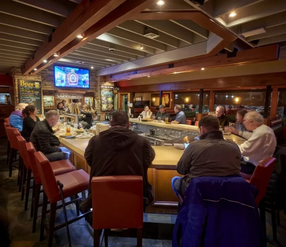 Patrons and a bartender at a restaurant bar during the evening.