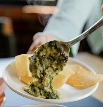 Spoon scooping steaming creamy green dip with chips.