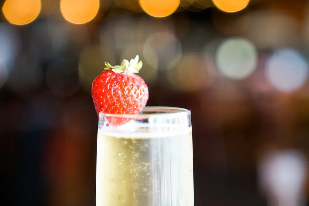 Bubbling golden drink in flute glass, garnished with a red strawberry.