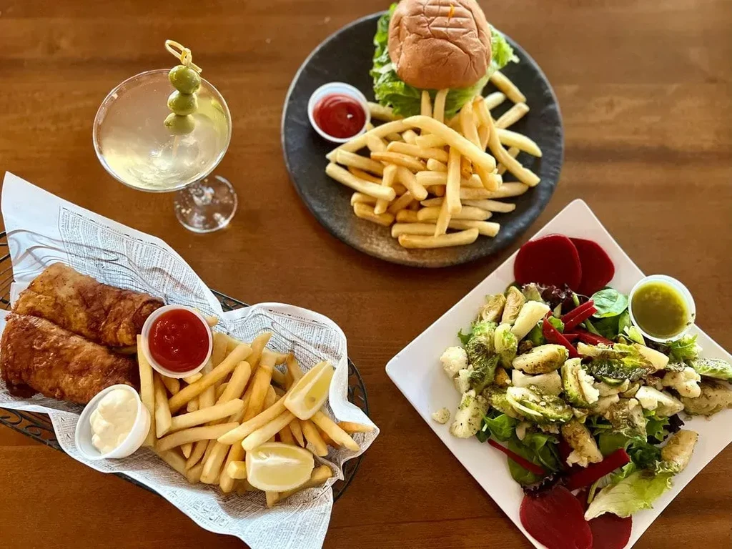 Fish and chips, burger, salad, and martini on a wooden table.