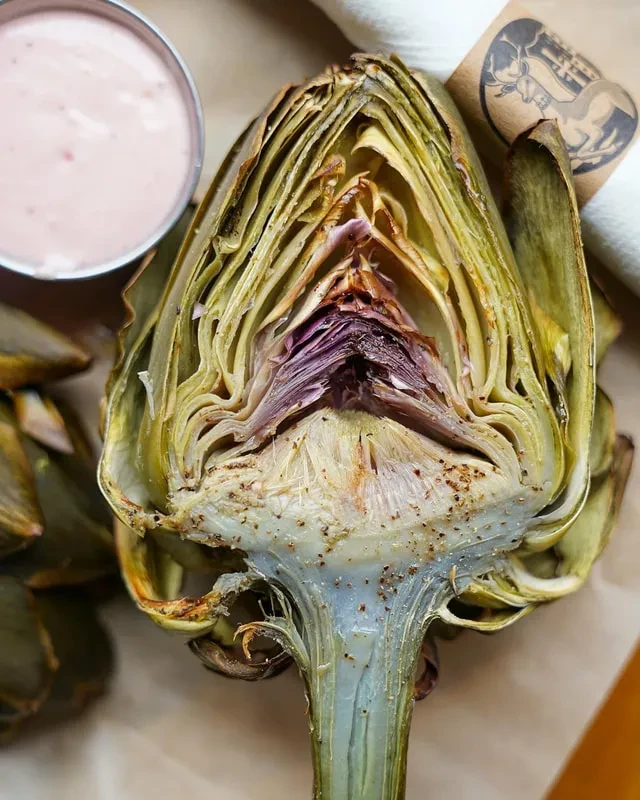 Cooked artichoke, halved lengthwise, with pink dipping sauce and napkin.