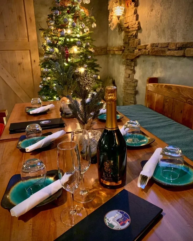 Restaurant table with champagne, animal-pin menu, decorated Christmas tree.