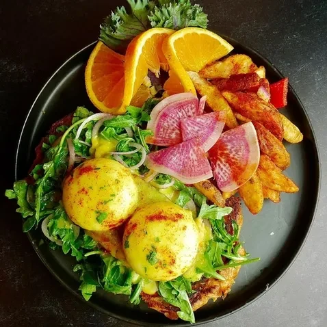 Plated poached eggs, arugula, potato wedges, watermelon radishes, and sauce.