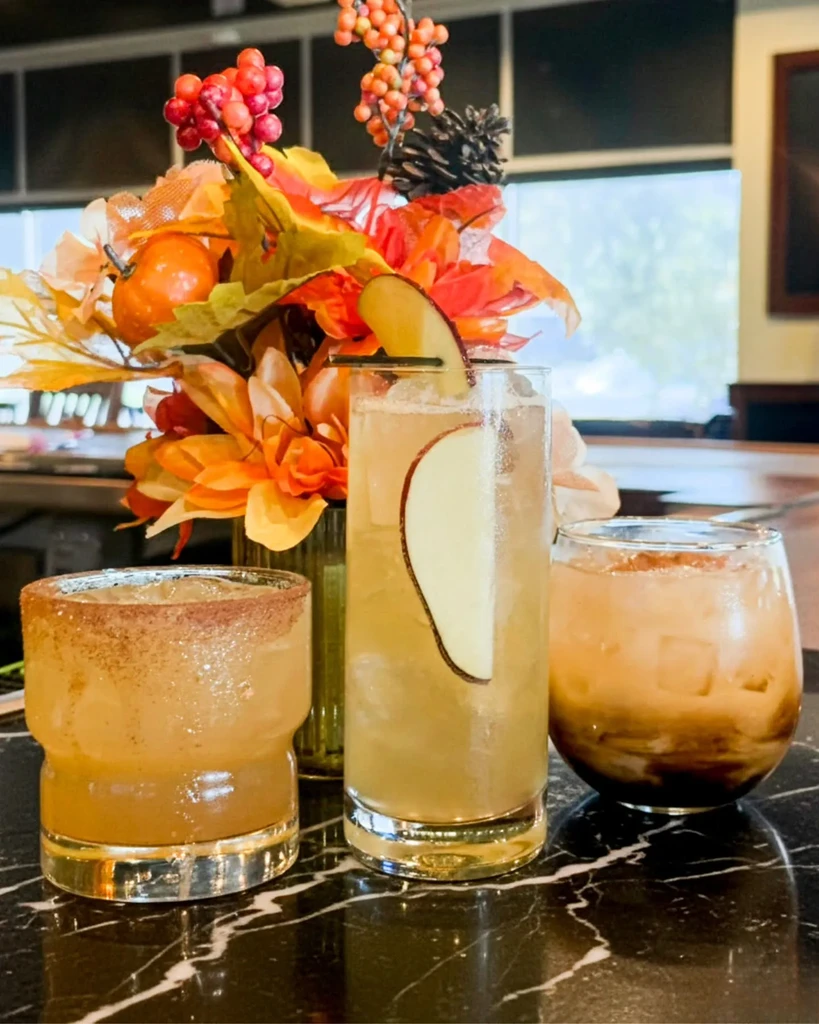 Three distinct drinks, one cinnamon-rimmed, with an autumn floral arrangement.