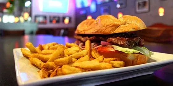 Cheesesteak sandwich, lettuce, tomato, onion, and french fries on a plate.