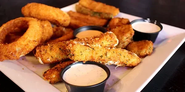 Assorted deep-fried appetizers with onion rings, mozzarella sticks, and dipping sauces.
