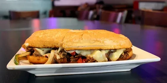 Cheesesteak sandwich with melted cheese, meat, onions, and peppers on a plate.