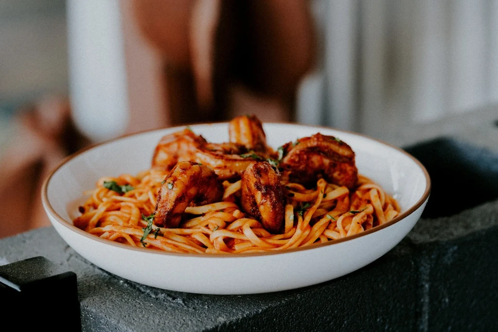 Pasta with reddish-orange sauce, caramelized shrimp/chicken, and fresh herbs.