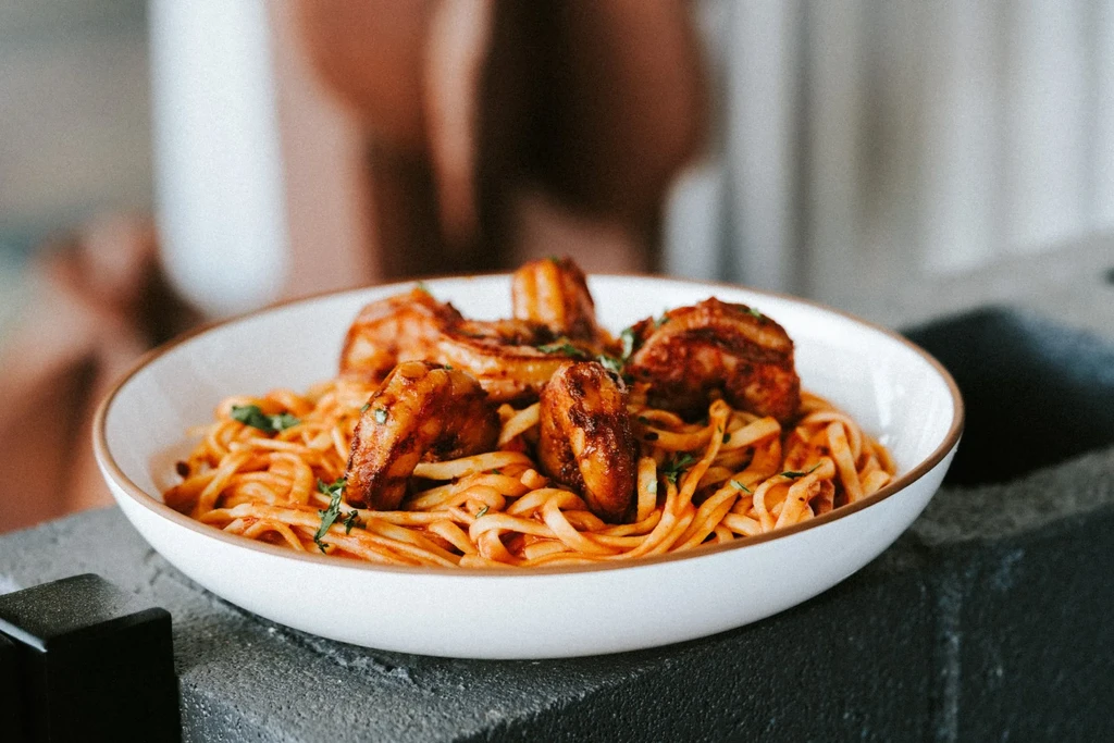 Close-up of pasta with reddish sauce, shrimp or chicken, and herbs.