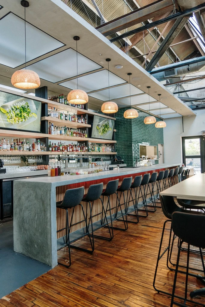Modern bar interior with a concrete counter, liquor shelves, and pendant lights.
