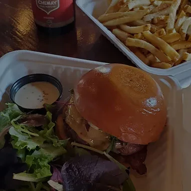 Burger with fries, salad, and sauce in disposable containers.