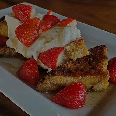 Golden French toast with syrup, whipped cream, and fresh strawberries.