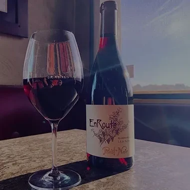 EnRoute Pinot Noir bottle and half-filled wine glass on table.